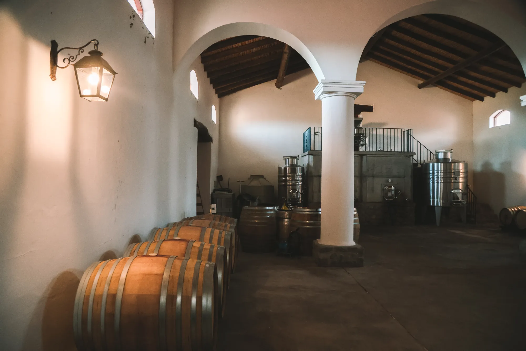 Warm-lit bodega interior with barrels, white arches, and vintage lantern